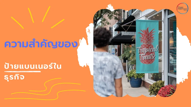 แบนเนอร์ธุรกิจสีเขียวที่มีข้อความ 'Tropical Treats' และภาพสับปะรดติดอยู่ด้านหน้าร้าน โดยมีผู้คนเดินผ่าน พร้อมข้อความ 'ความสำคัญของป้ายแบนเนอร์ในธุรกิจ'